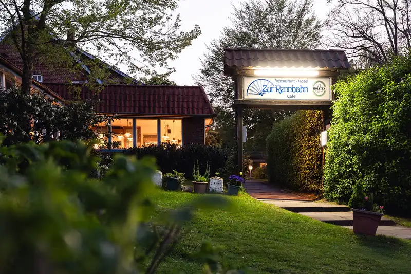 Eingang des Hotel Zur Rennbahn mit beleuchtetem Schild am Abend